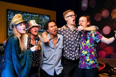 Five friends in sequinned hats singing arm in arm
